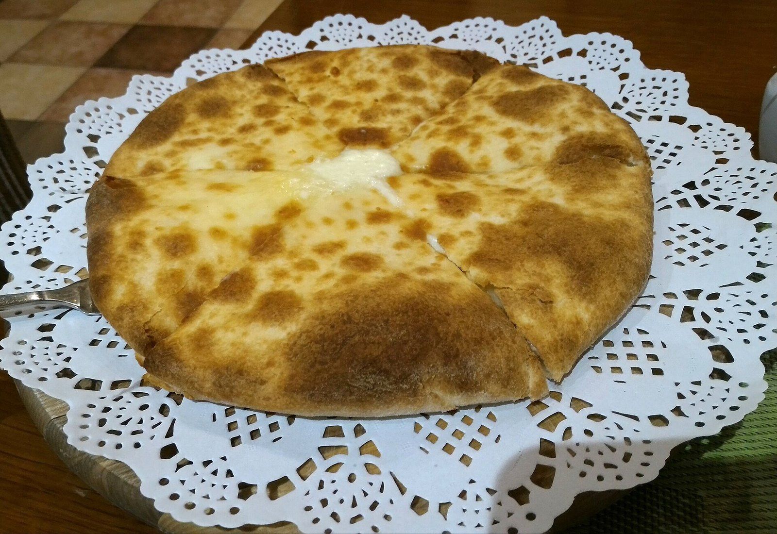 Круглый хачапури с румяной пятнистой корочкой, разрезанный на четыре части, с расплавленным сыром в центре