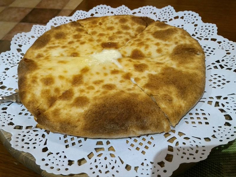 Круглый хачапури с румяной пятнистой корочкой, разрезанный на четыре части, с расплавленным сыром в центре