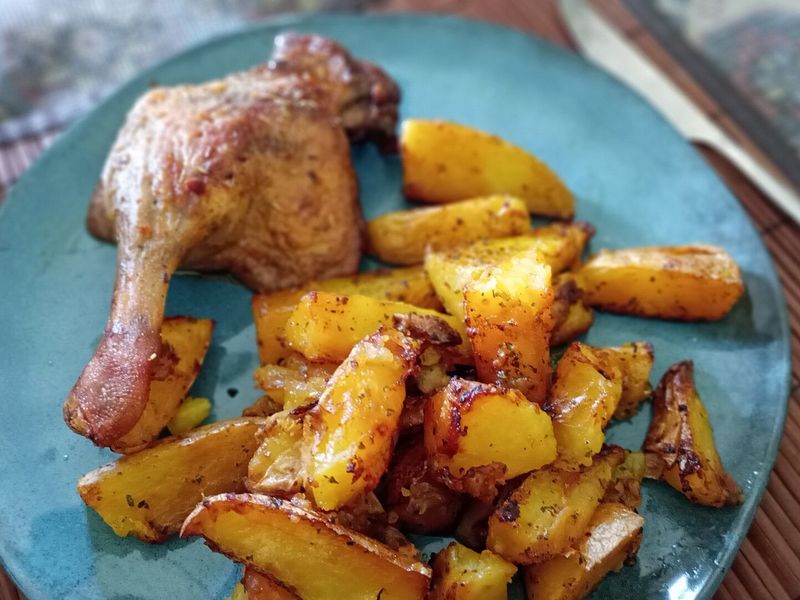 Запечённый куриный окорочок с румяным картофелем дольками на тарелке