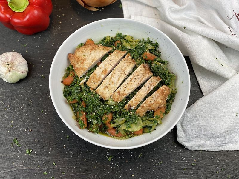 Нарезанная куриная грудка на тушёном шпинате с морковью