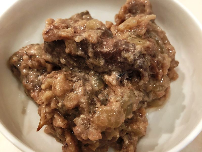 Кусочки печени с луком в сметанном соусе в белой миске
