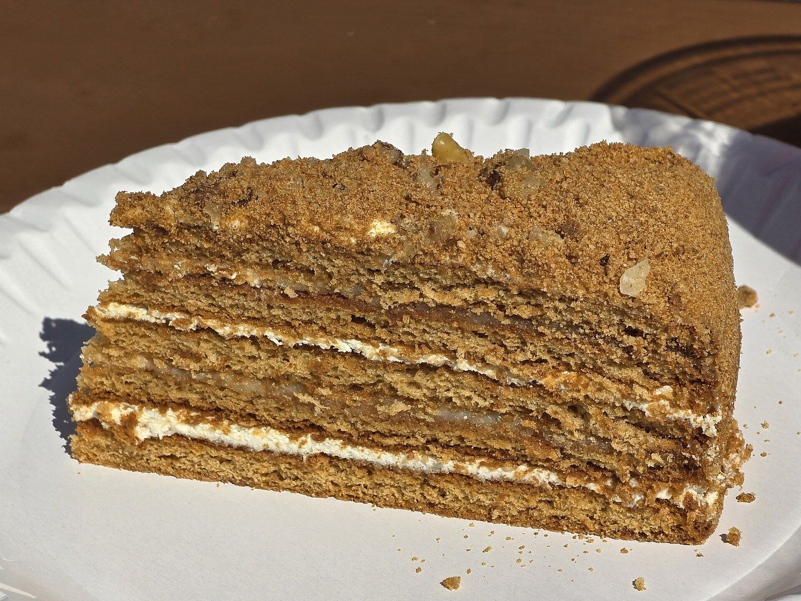 Кусок медовика — тонкие медовые коржи, белый крем и посыпка из крошки с орехами