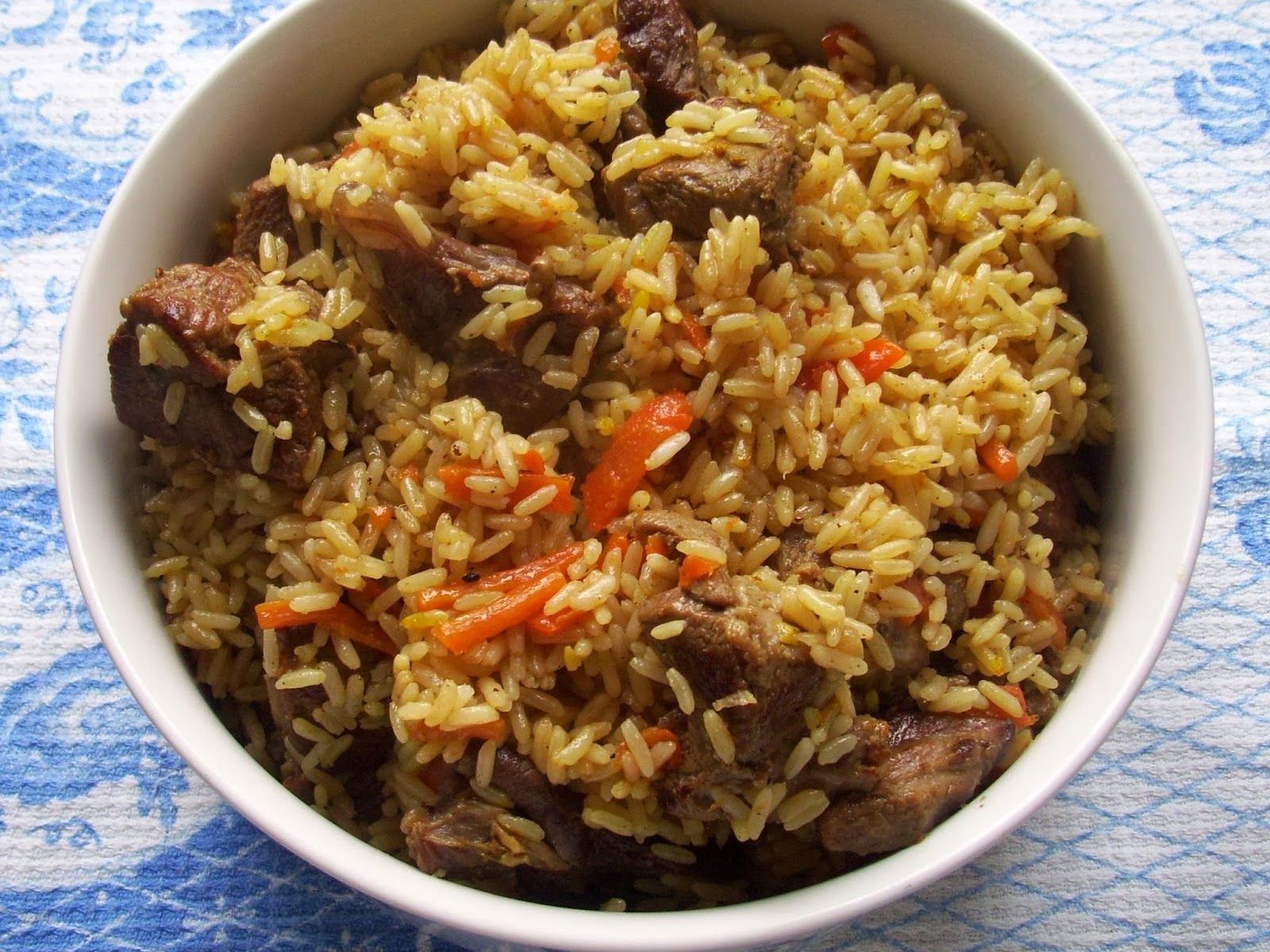 Домашний плов с кусками мяса и морковью соломкой в белой миске