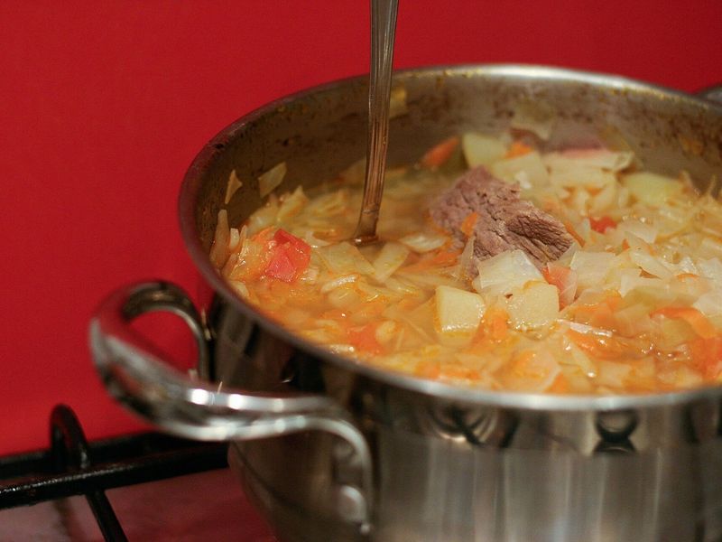 Щи из свежей капусты с говядиной, картофелем и помидорами в кастрюле на плите