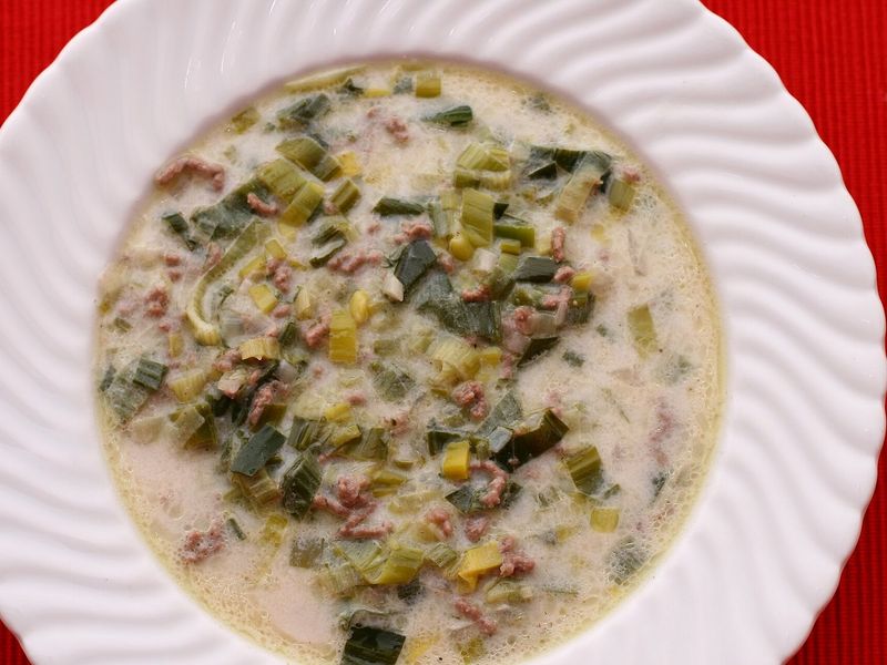 Сырный суп с луком-пореем и фаршем в белой тарелке
