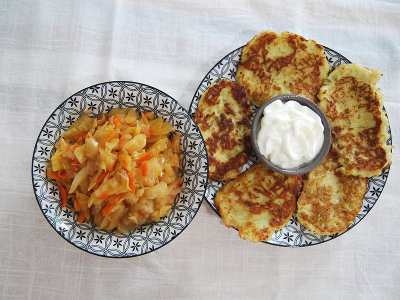 Тушёная капуста с морковью в миске, рядом драники со сметаной