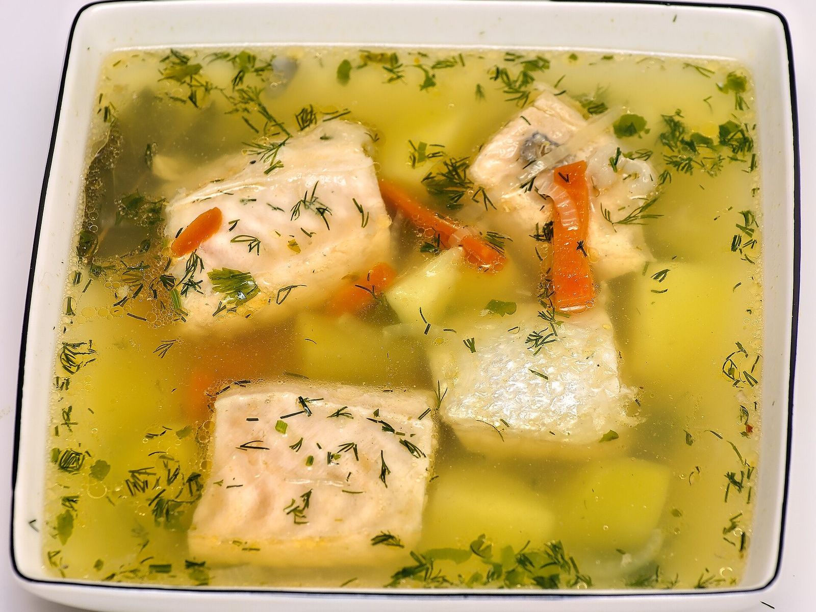 Уха с крупными кусками красной рыбы, картофелем, морковью и укропом в квадратной тарелке