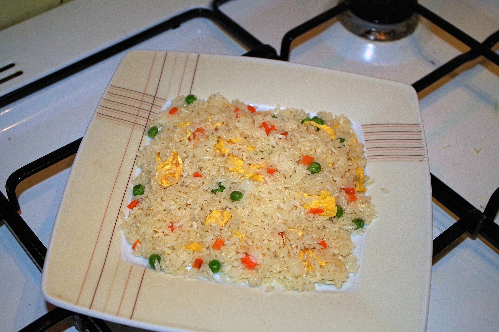 Жареный рис с кусочками яйца, зелёным горошком и морковью на квадратной тарелке