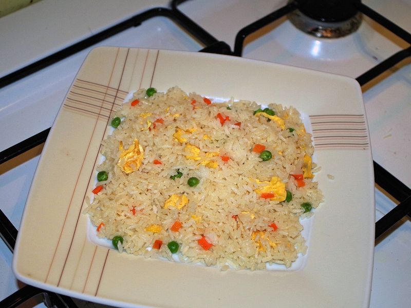 Жареный рис с кусочками яйца, зелёным горошком и морковью на квадратной тарелке